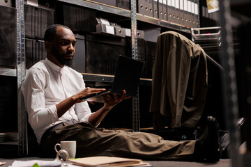Private detective conducting investigation using laptop while sitting on floor surrounded by police report papers. Detective analyzing crime case information on computer in evening