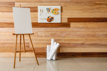 Easel and pegboard with drawing tools on wooden wall in studio