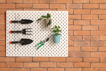 Pegboard with gardening tools and plants on brick wall