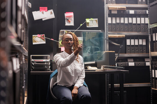 African american detective examining holographic image in evidence room, investigating clues and insight. Female investigator working with augmented reality and artificial intelligence.