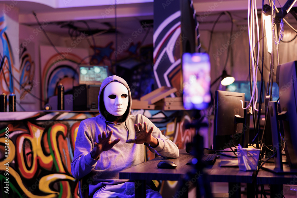 Poster hacker in anonymous mask live streaming illegal content online on mobile phone. criminal recording r