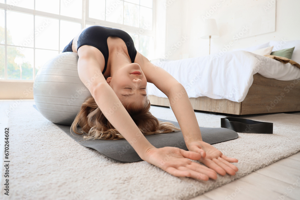 Poster Young sporty woman stretching with fitness ball during training at home