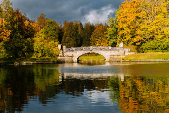 Viskontiev Bridge over the Slavyanka River in autumn in Pavlovsky Park. Nature autumn landscape. Colorful autumn foliage and river in park. Autumn trees were reflected in the water.
