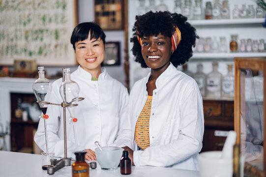 Portrait of multiracial chemists standing in a vintage apothecary with lab vessels.