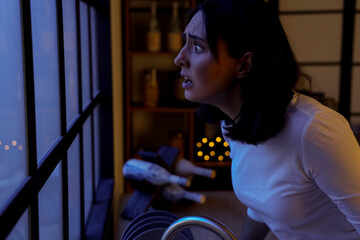 Beautiful young afraid woman in evening near window at kitchen