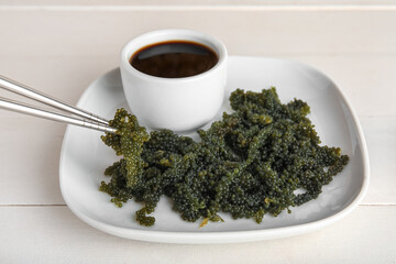 Plate with healthy seaweed and soy sauce on light wooden background