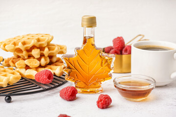 Bottle and bowl of sweet maple syrup with raspberries on white background