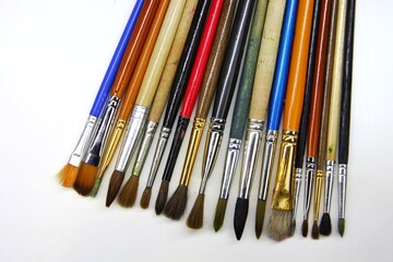 Fototapeta premium Many art brushes Lying on a white plane of different sizes and colors lie in a row sideways to each other. Different brushes for painting with oils, watercolors and gouache. beautiful background