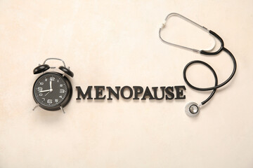 Word MENOPAUSE with alarm clock and stethoscope on light background