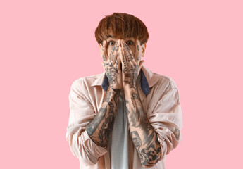 Afraid young tattooed man on pink background