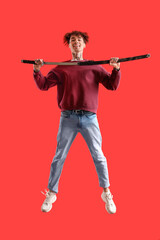 Tattooed young man with sword jumping on red background