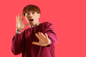 Afraid young tattooed man on red background