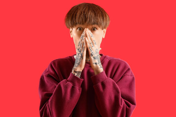 Afraid young tattooed man on red background