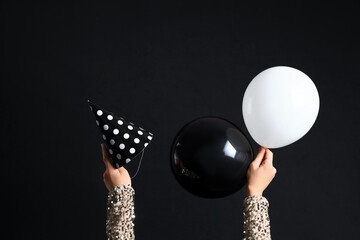 Female hands with party cone and balloons on black background