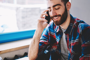 Cheerful bearded young man talking with friend on smartphone using high speed mobile connection