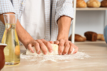 Obraz na płótnie Canvas Young man preparing dough for fresh buns at table in kitchen, closeup