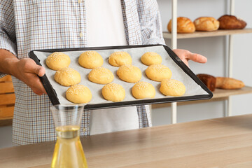 Handsome young man holding tray with fresh raw buns in bakery