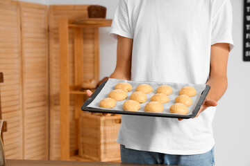 Handsome young man with tray of fresh raw buns in bakery