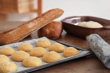 Fresh bread and tray with raw buns on table in bakery