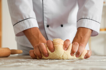 Handsome young chef kneading dough for bread at table in bakery