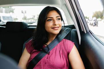 Happy young adult indian woman traveling by car, sitting in the back seat of a taxi