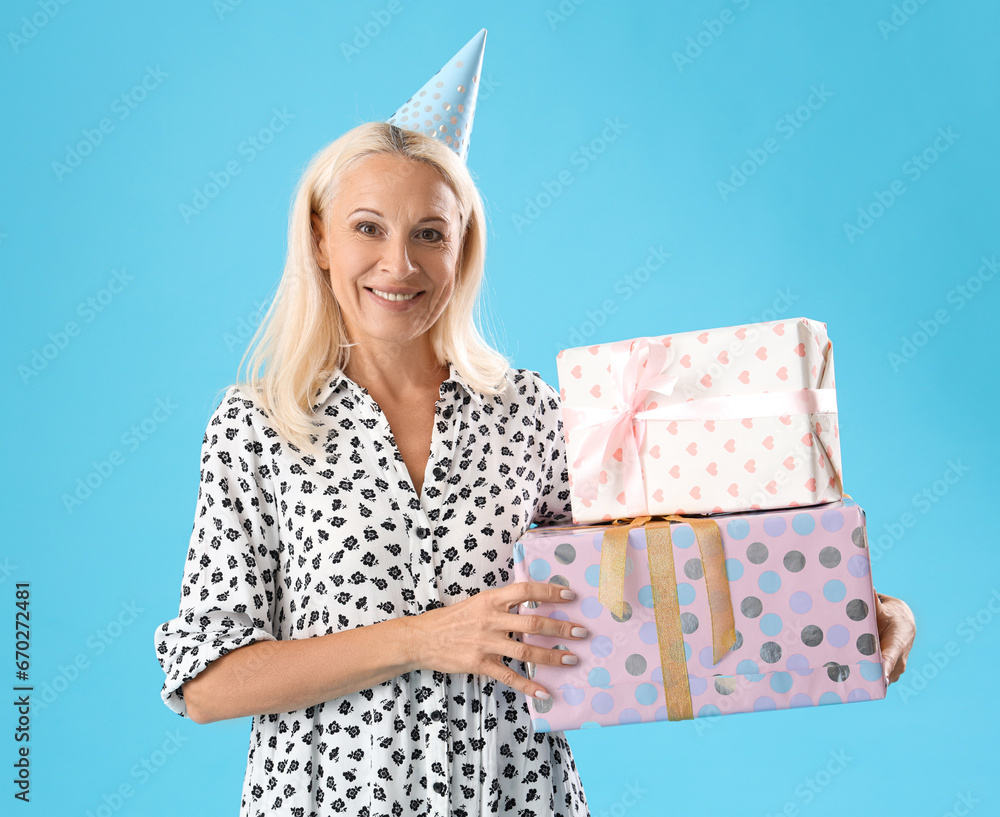 Poster Happy mature woman in party hat with gift boxes on blue background