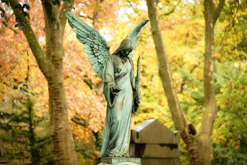 an antique angel figure with a palm branch stands on a grave of a cemetery in front of an autumnal...