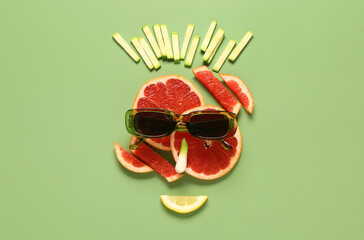 Funny face made of fruits, vegetables and sunglasses on green background