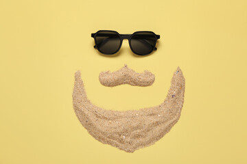 Funny face made of sand and stylish sunglasses on color background