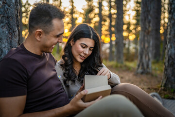 Young couple man and woman give present gift box while sit in nature