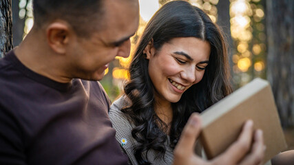 Young couple man and woman give present gift box while sit in nature