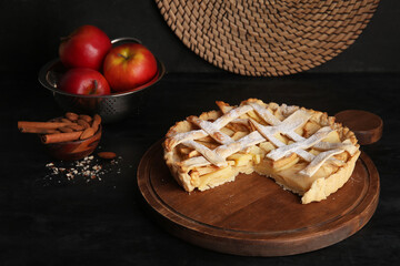 Wooden board of delicious apple pie with almond and cinnamon on black background