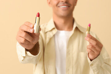 Male makeup artist with lipsticks on beige background, closeup