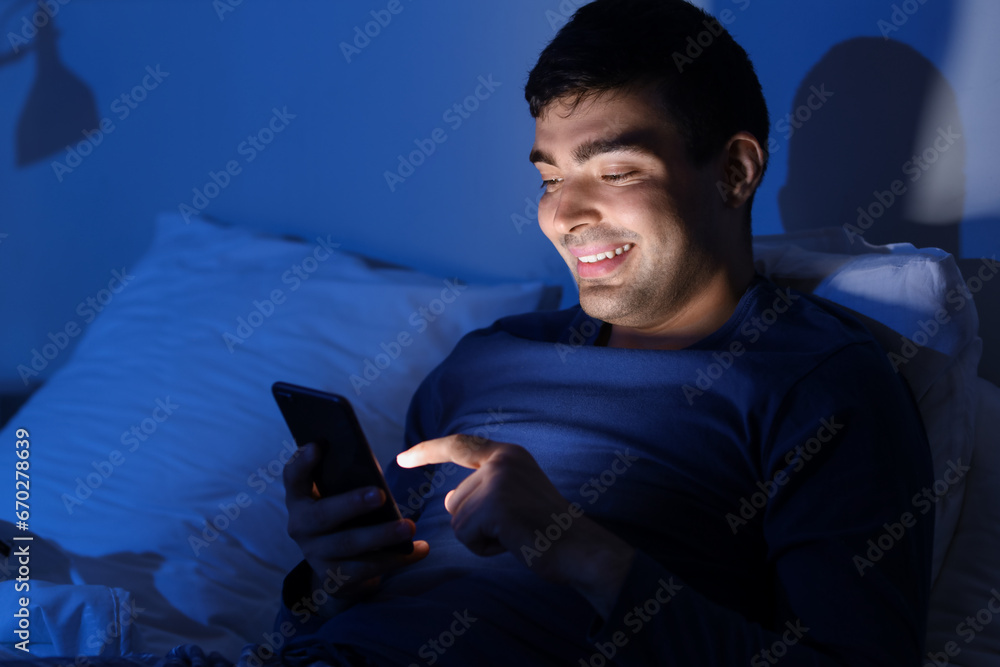 Sticker Young man using mobile phone in bed at night