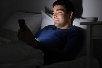 Fototapeta premium Young man using mobile phone in bed at night