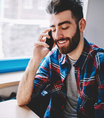 Cheerful bearded young man talking with friend on smartphone using high speed mobile connection