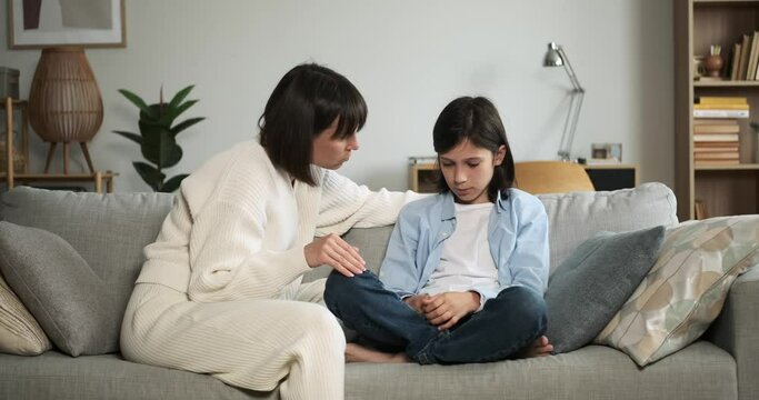 Worried mother attentively listens to sad son while they sit together on the couch. Her empathetic expression reflects care and support as they share a moment of emotional conversation.