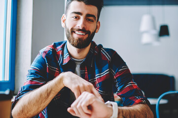 Cheerful hipster guy dressed in casual wear managing time on wristwatch