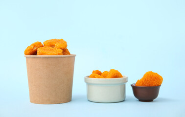 Paper bucket and bowl of tasty nuggets with ketchup on blue background