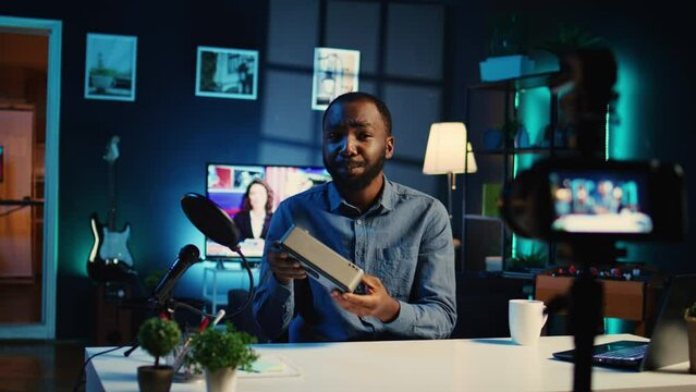 Content creator doing technology review of portable speaker for online streaming channel in home studio. Influencer films music playing device unboxing for his audience in cozy apartment