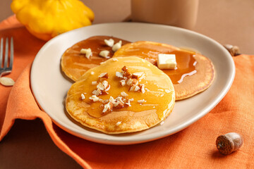 Plate of tasty pumpkin pancakes with piece of butter, honey and nuts on brown background