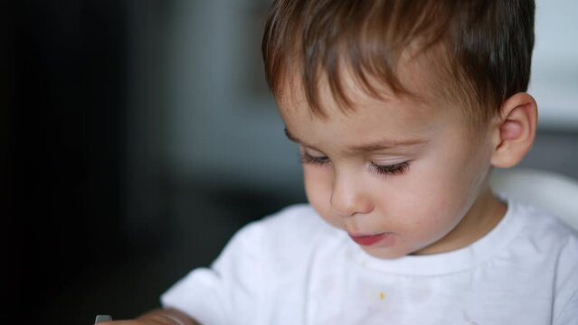 Sweet Caucasian baby boy having meals. Adorable kid looks at camera. Close up. Blurred backdrop.