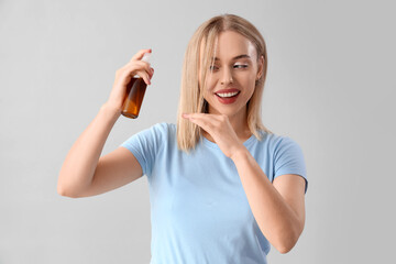 Young blonde woman applying hair spray on light background