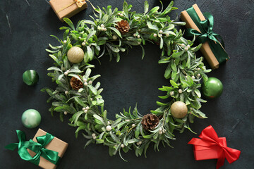 Christmas mistletoe wreath with balls, cones and gift boxes on dark background