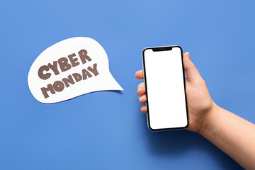 Female hand with modern mobile phone and text CYBER MONDAY on blue background