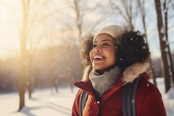 Obraz premium A young african american woman is playing in the snow happily with a winter coat and a winter hat in a in snow covered forest during sunset in winter on a bright day