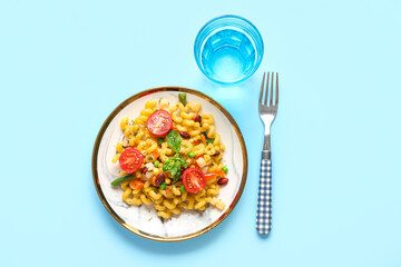 Plate with tasty pasta primavera and glass of water on blue background