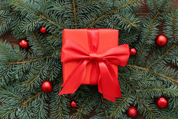 Gift box with Christmas tree branches and balls on wooden background, closeup