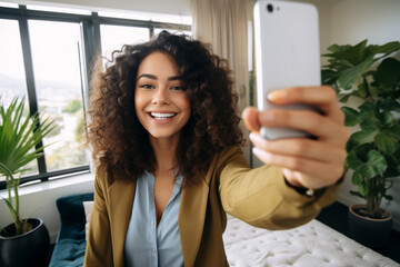 A young latin woman is is making a selfie while smiling with a telephone in a modern living room a high tech social media woman - obrazy, fototapety, plakaty