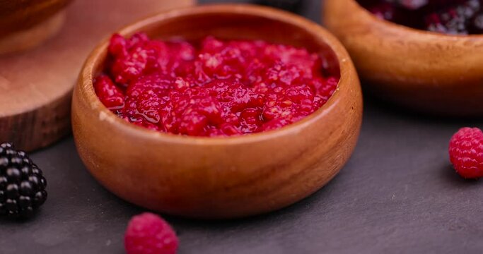 crumpled juicy red raspberries in a wooden bowl, crumpled raspberries on the table during cooking